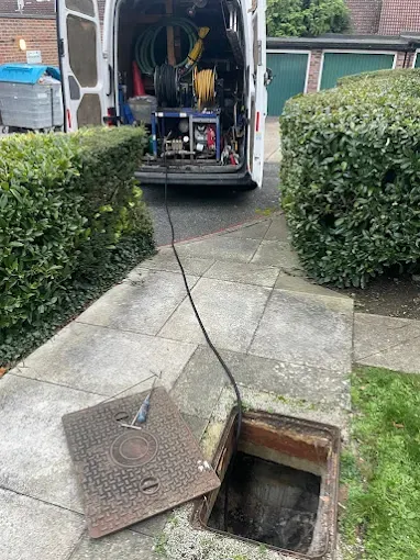 Open inspection chamber with a jetting hose feeding in, equipment van behind in a suburban garden